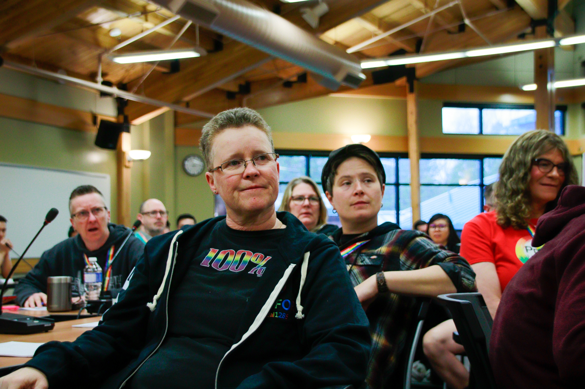 Attendees sitting in a room, listen to a person speaking.