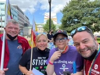 Four people standing together smiling holding flags at a rally.