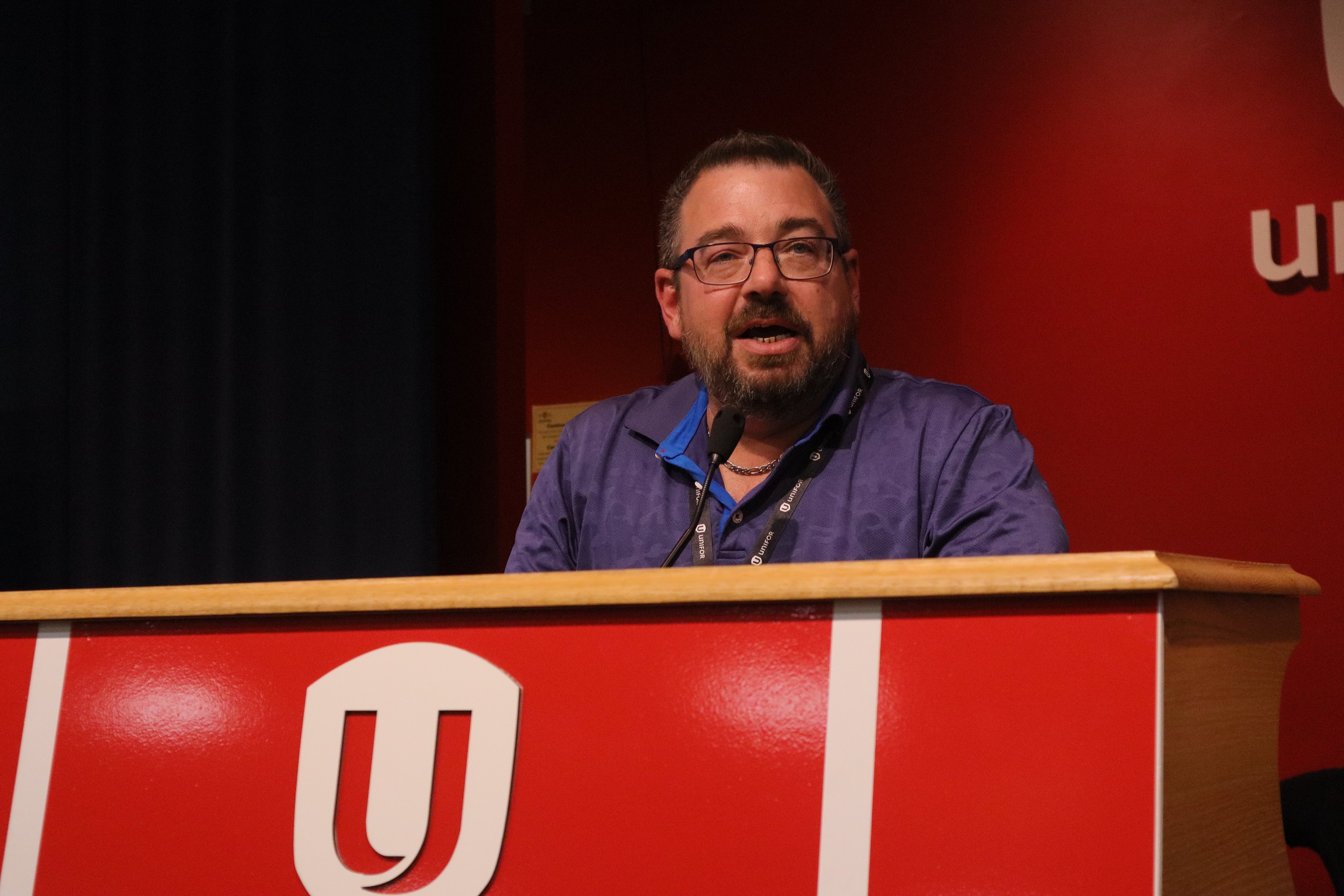 A man speaking at a podium the the Unifor shield.