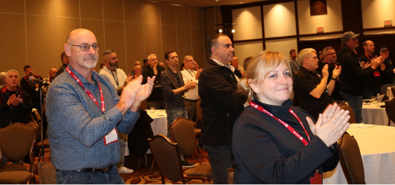 People in a room standing and clapping with a woman and a man in the foreground