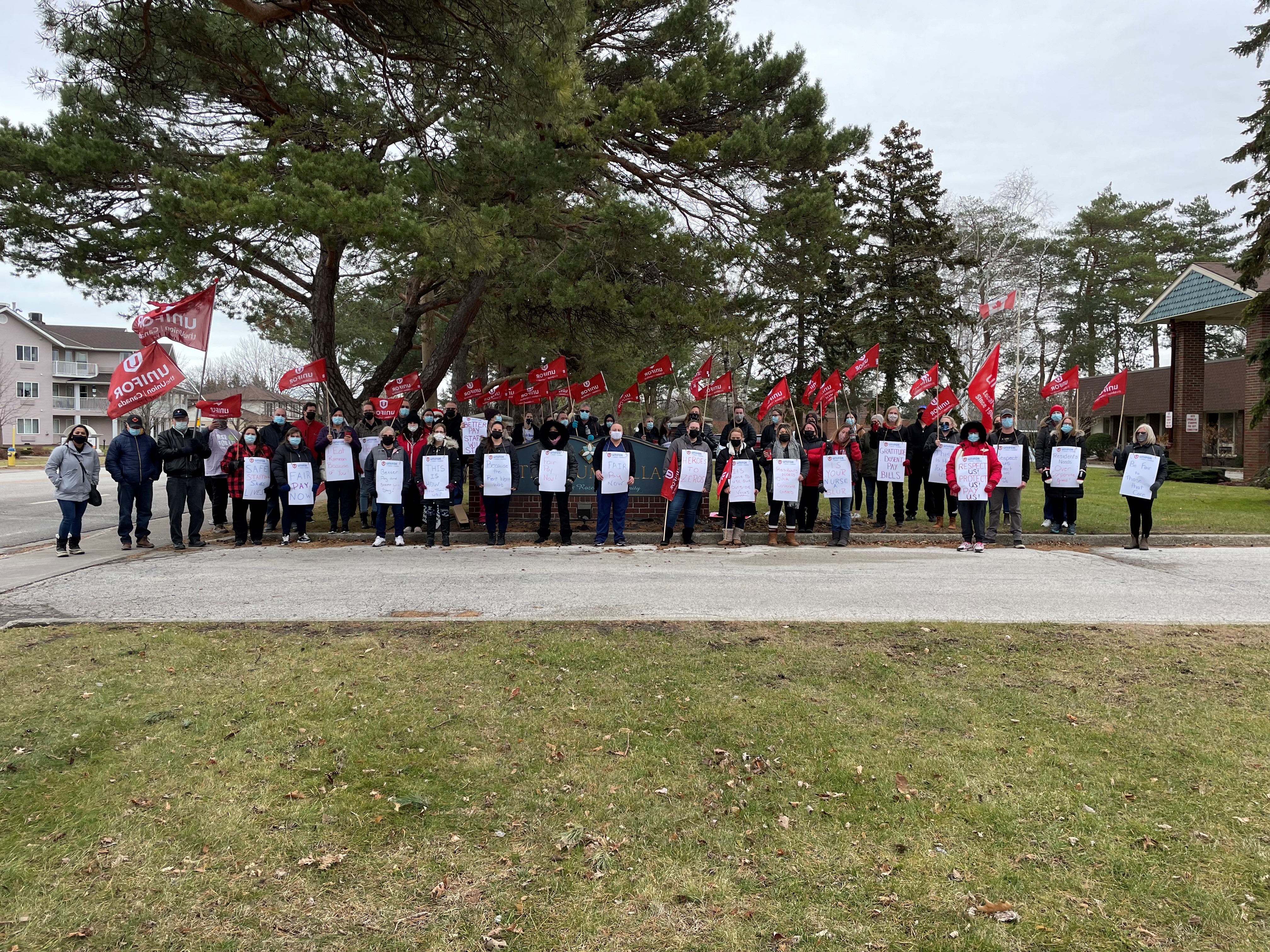 Large group of long-term care workers stand holding placards and flags