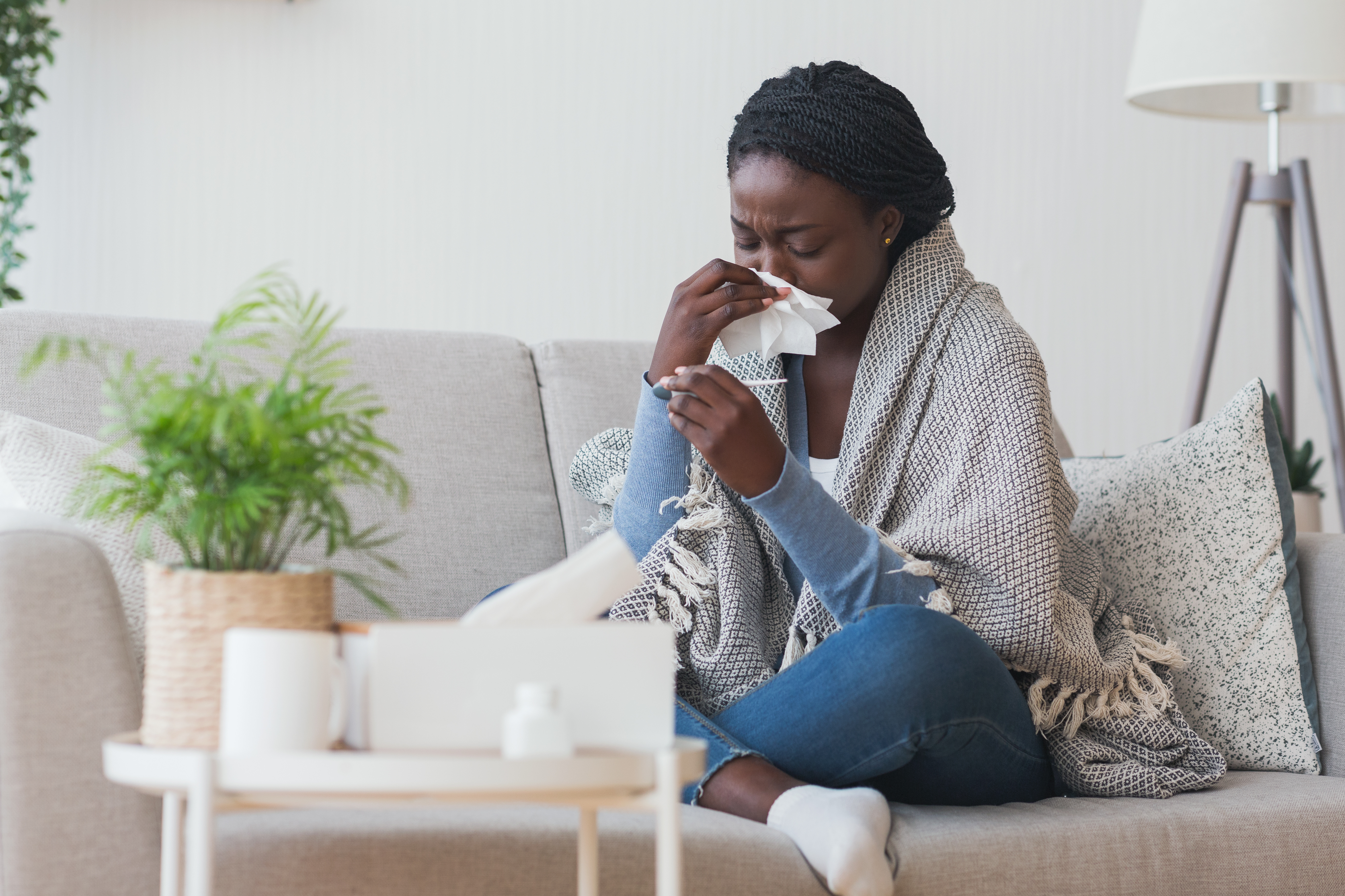 Femme sur un canapé s'essuyant le nez avec un mouchoir et regardant un thermomètre
