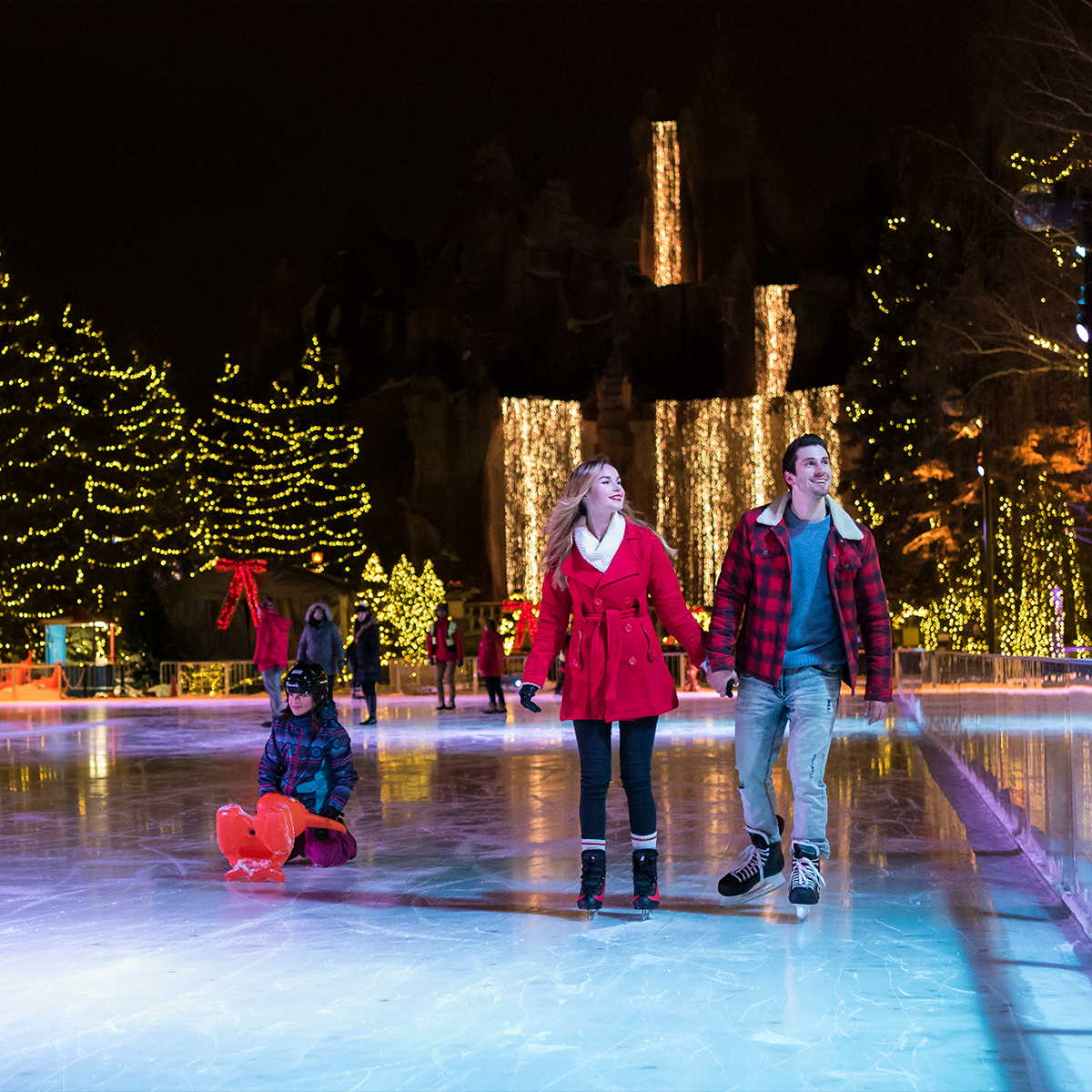 A couple ice skating, lights all around 