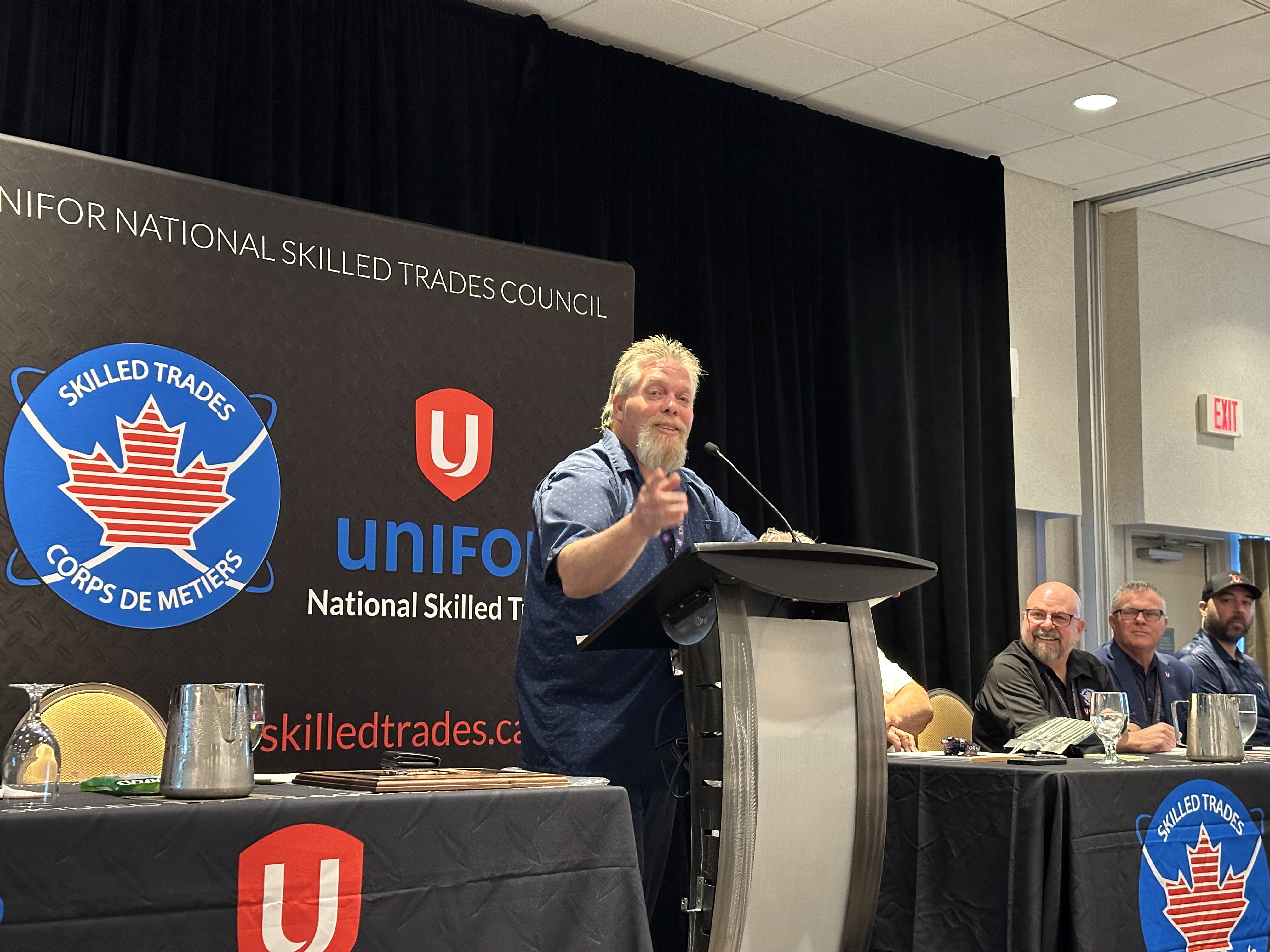 Man standing at a podium pointing out into the room.