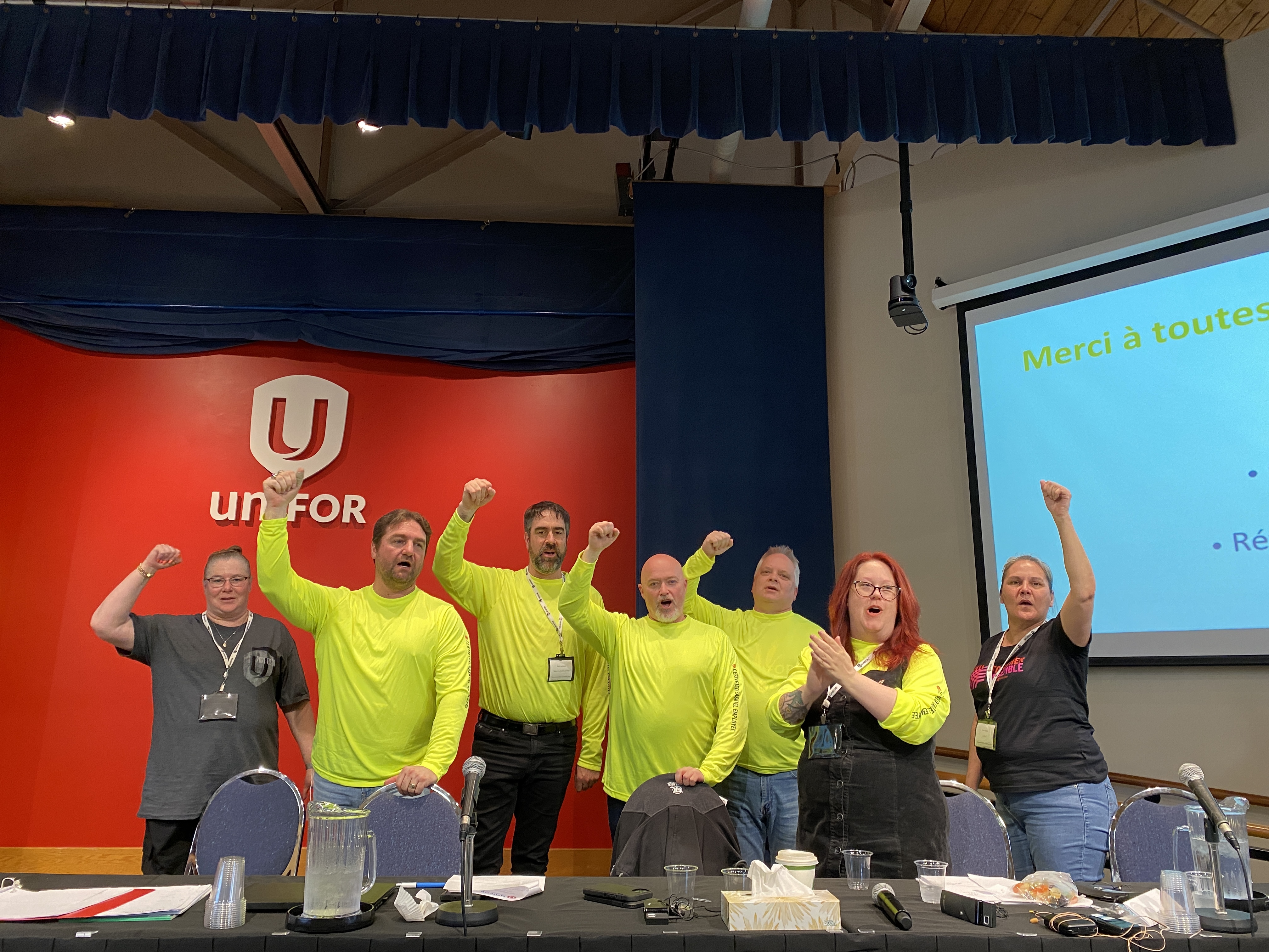 Sasktel group standing wearing yellow shirts with fists in the air.