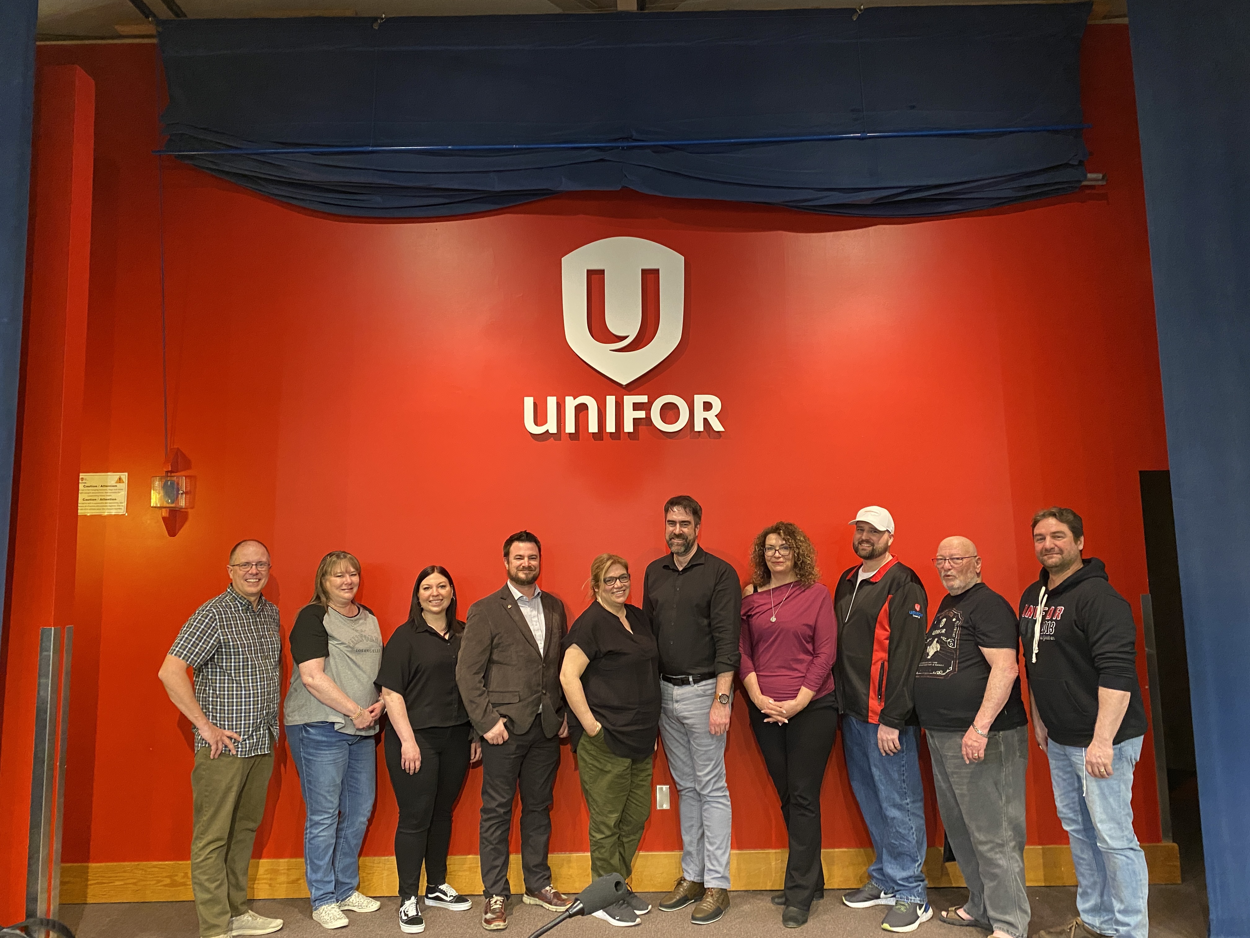 Telco executive committee standing in front of a red Unifor banner