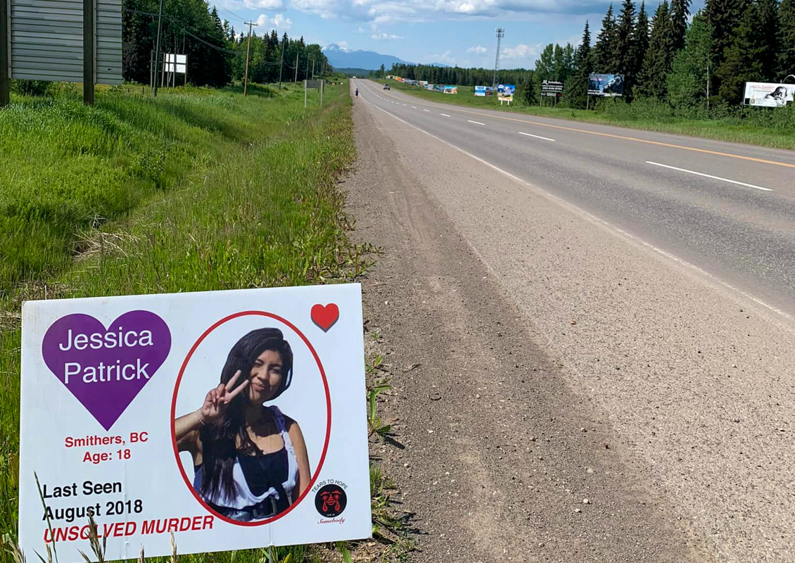 Road sign in foreground with photo of woman and 'unsolved murder' text below. Highway stretching into the distance.