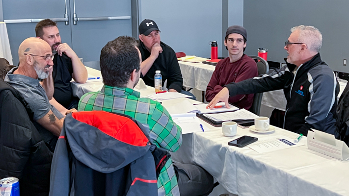 Six people seated on either side of a thing table talking.