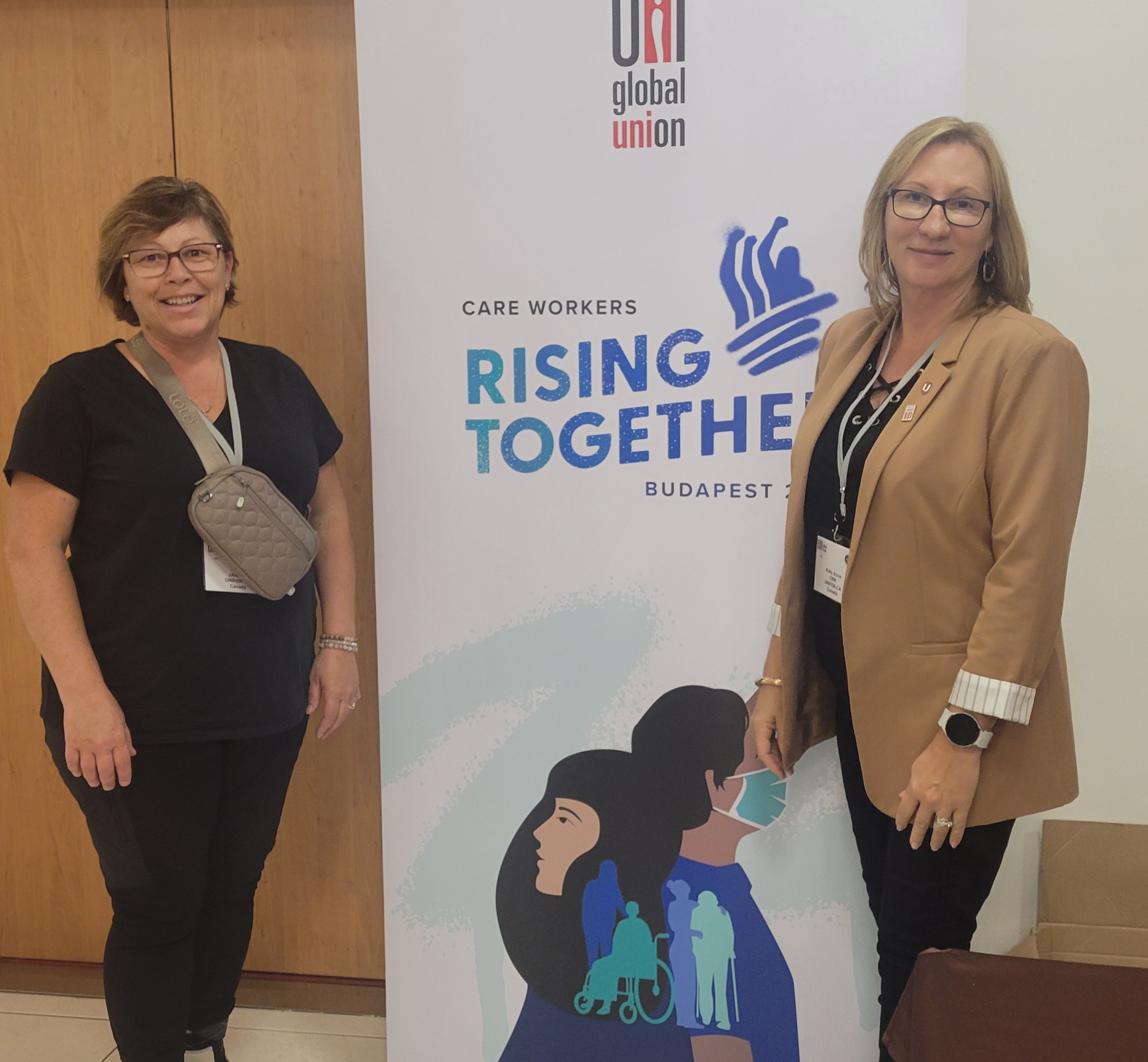 Two women standing aside a pop up banner, rising together