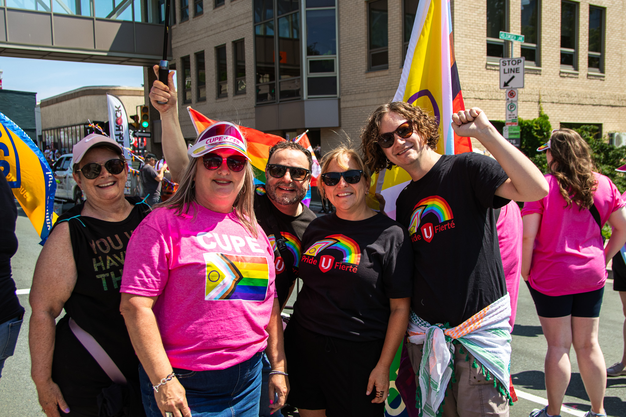 Five people wearing Pride shirts smiling some have fists raised