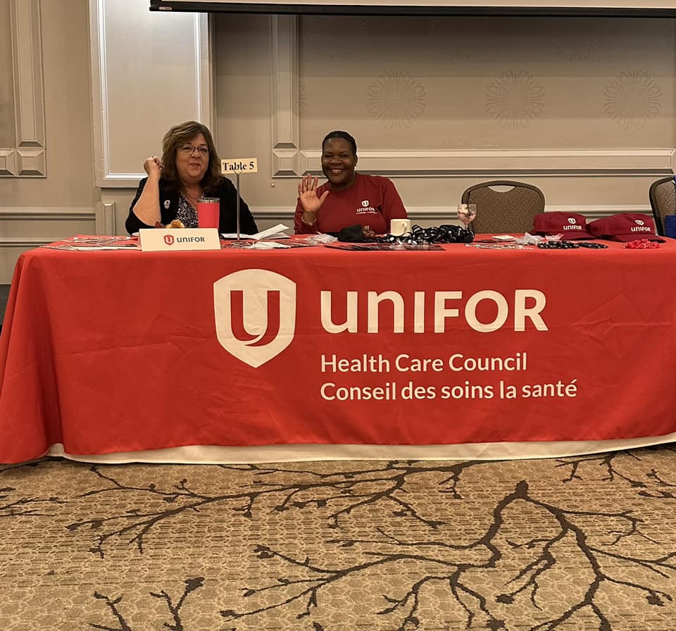 two women sitting at a table with a Unifor Health Care logo on the red table cloth