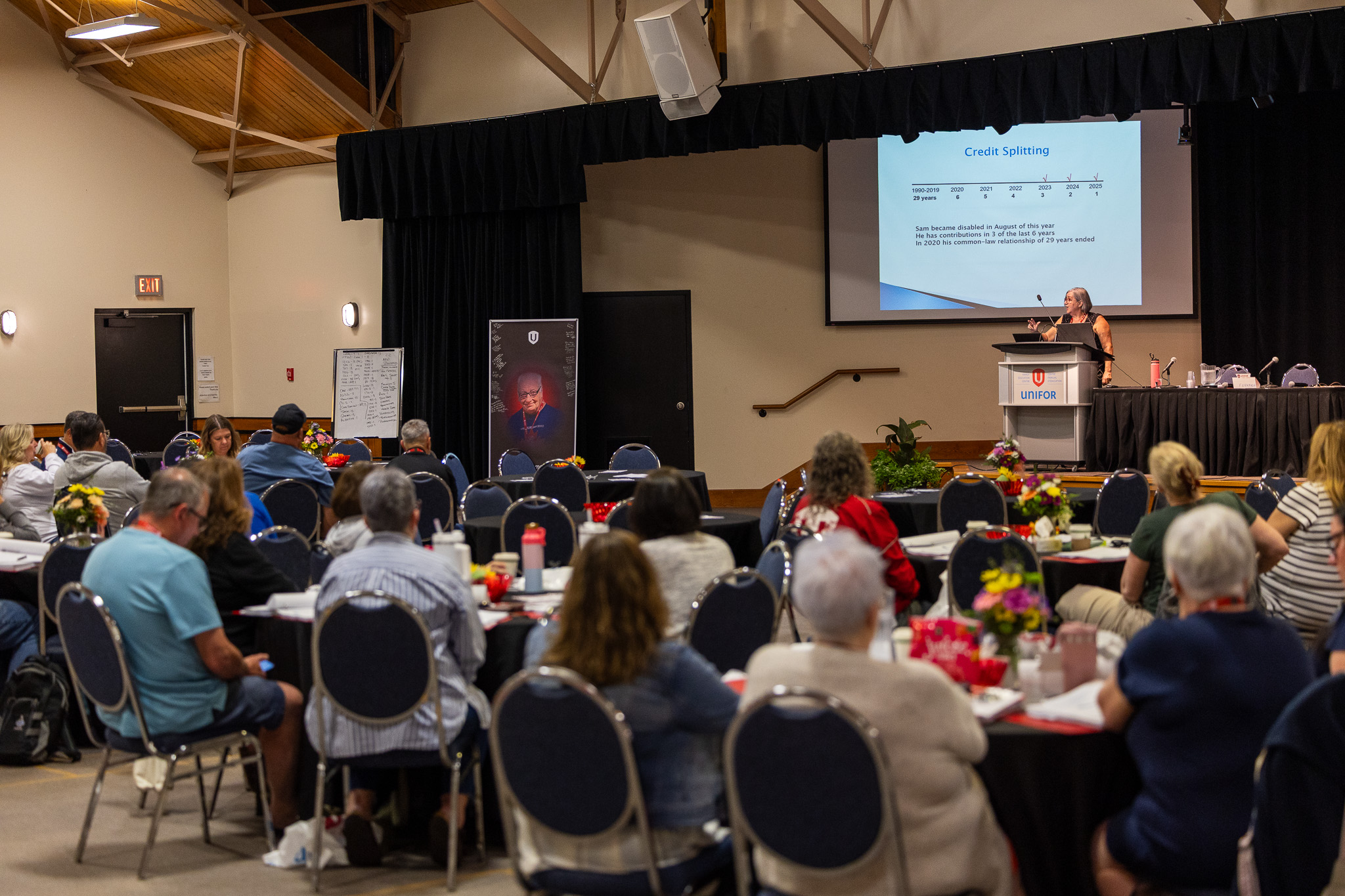 back room view of a conference looking at a presentation screen and women speaking