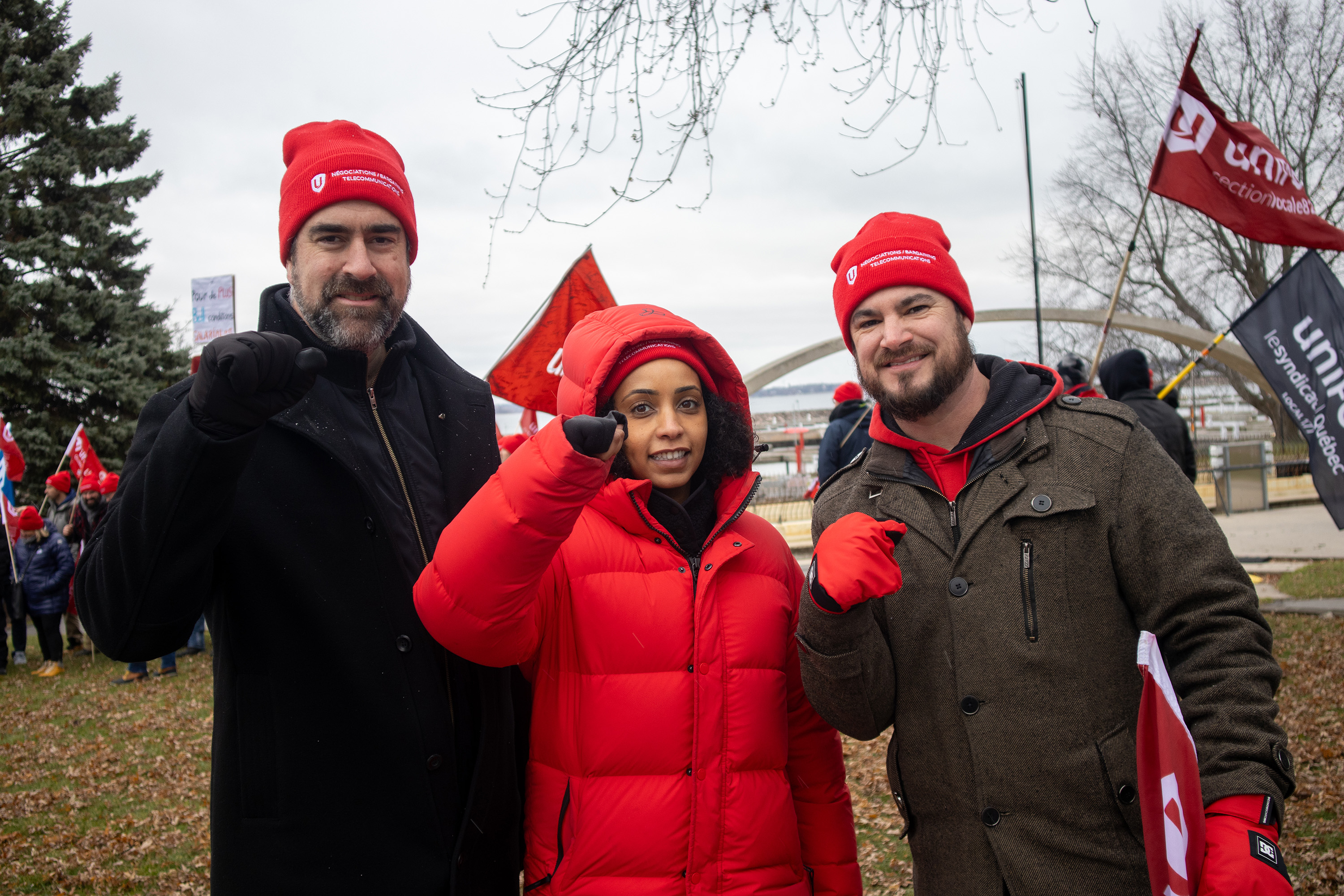 Three people standing outside in winter coats and hats smiling.