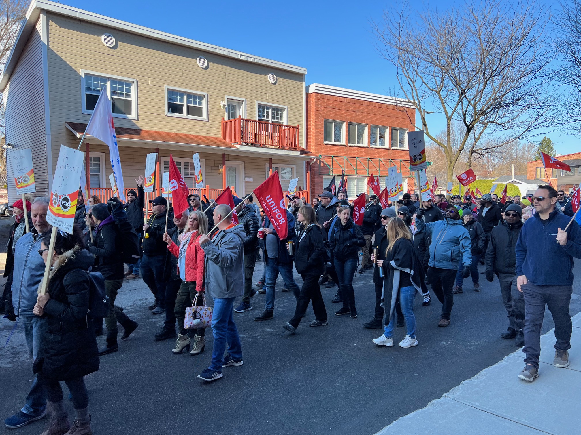 A group of people march down the street, carrying PSAC picket signs.