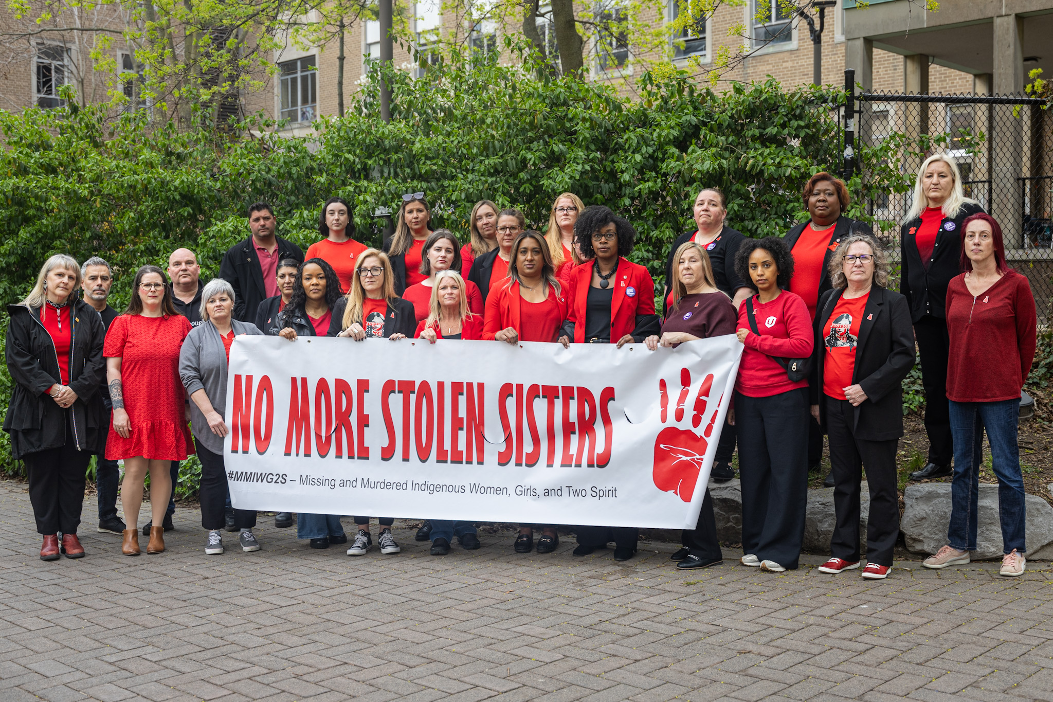 Women wearing red shirts hold a banner that reads: no more stolen sisters