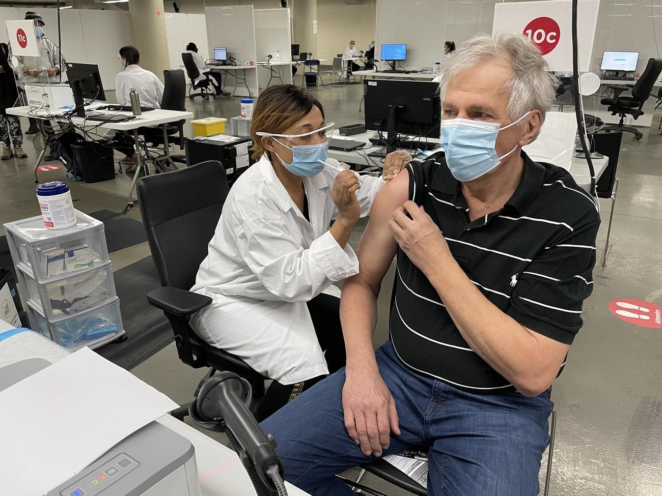 Renaud Gagné wears a mask while receiving a vaccination from a health care worker in a mask and faceshield.