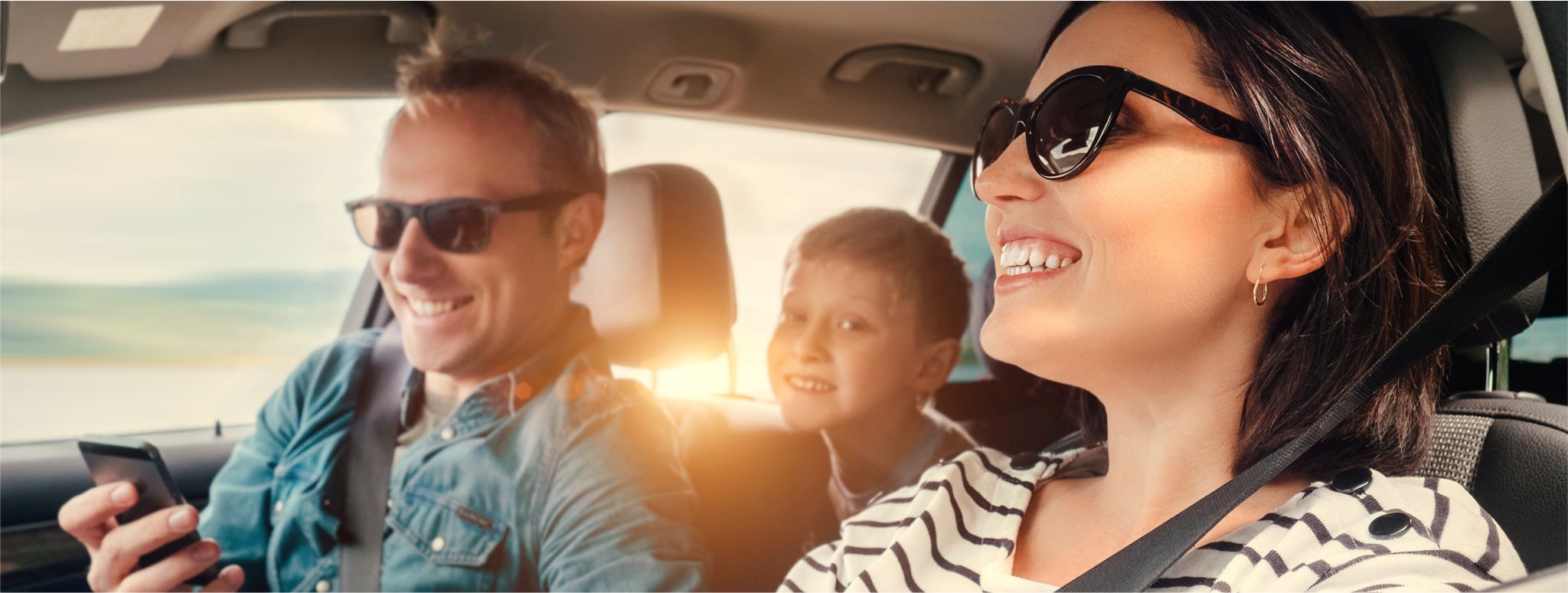 A family driving in a car wearing sunglasses smiling