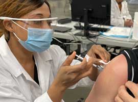 A nurse wearing PPE putting a needle vaccine in an arm