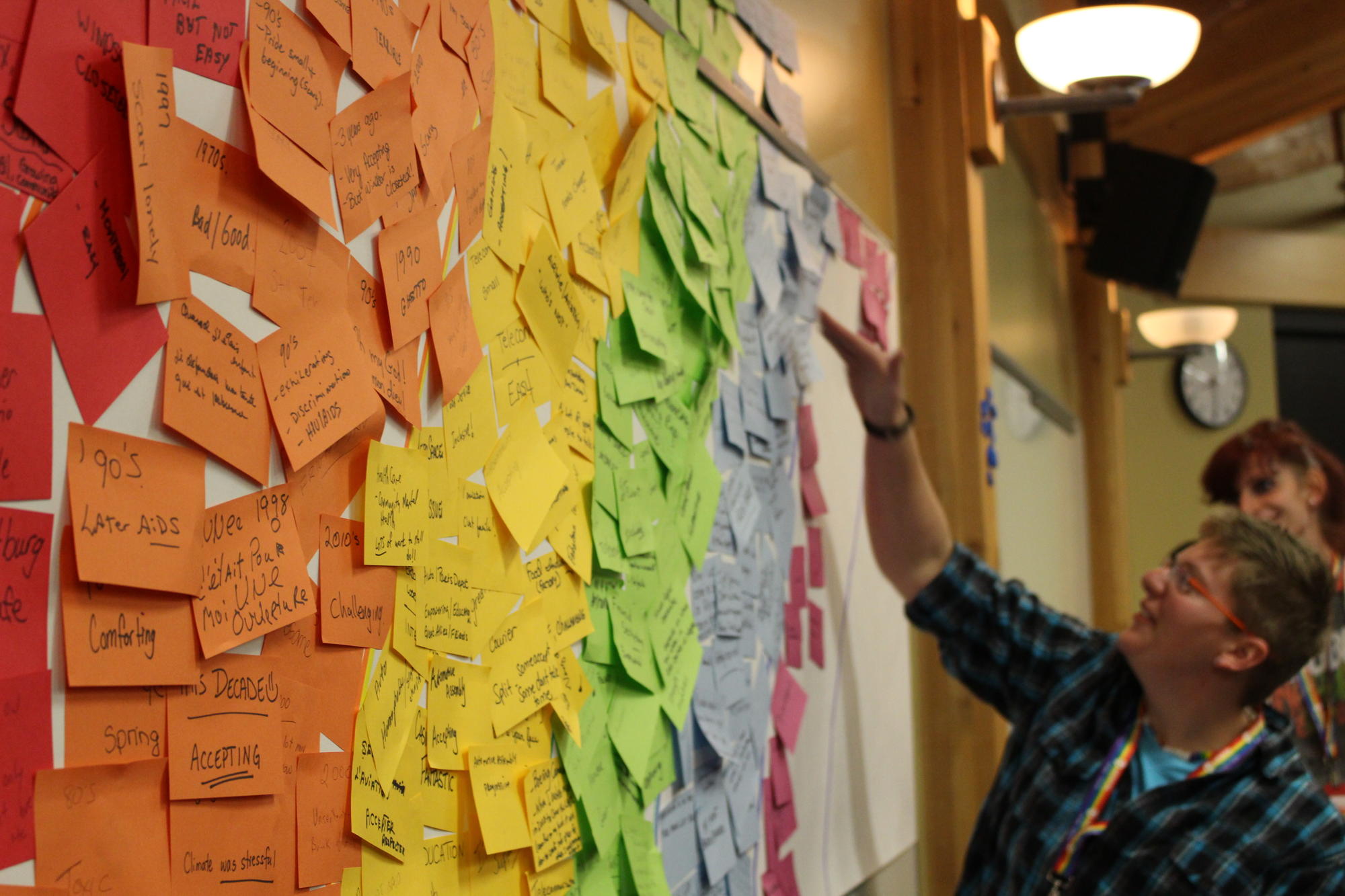 A Unifor member reads messages written on a rainbow of colourful post-its posted on a wall.
