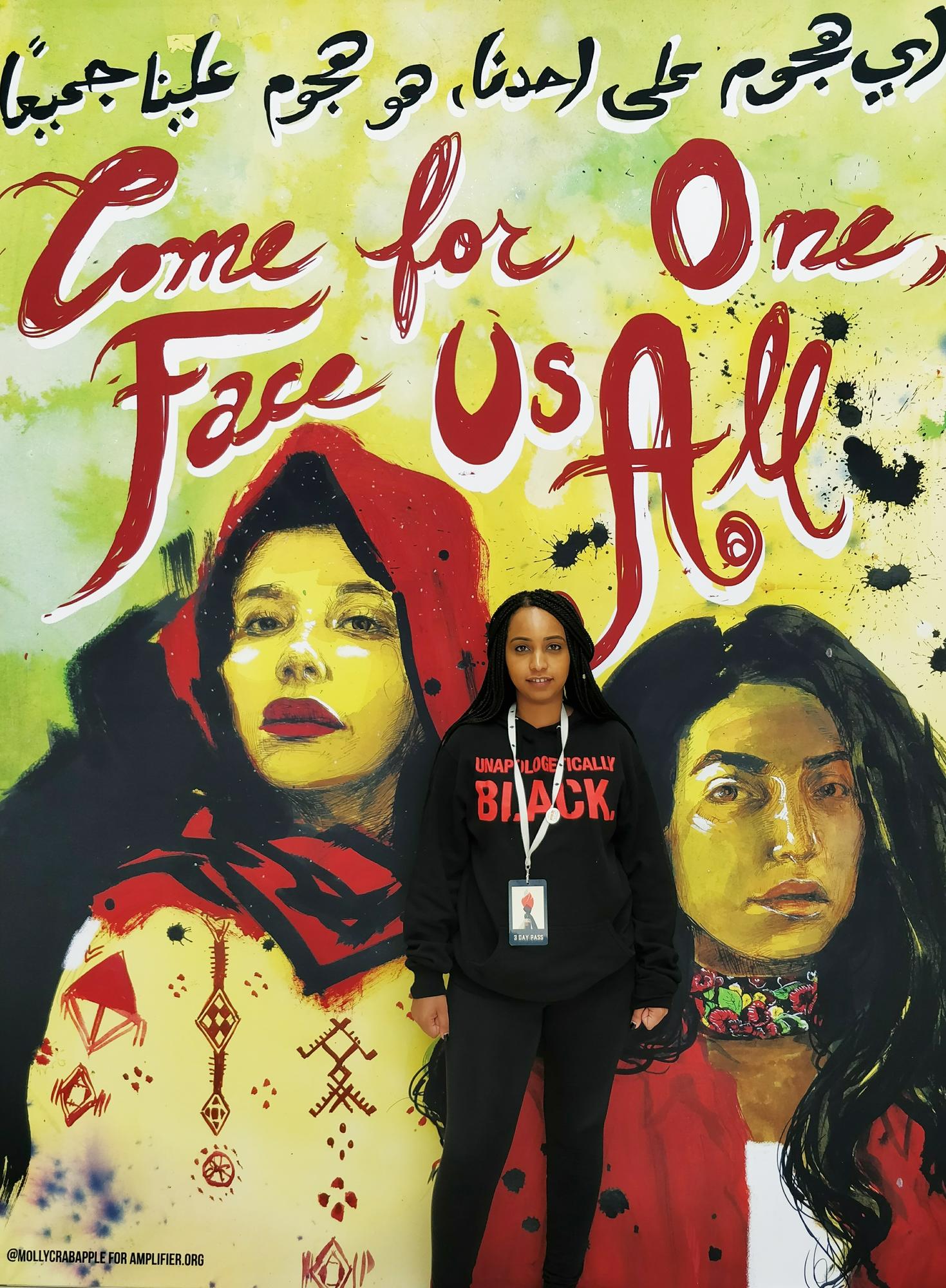 Samia Hashi of Unifor Local 6006 poses in front of a large mural.