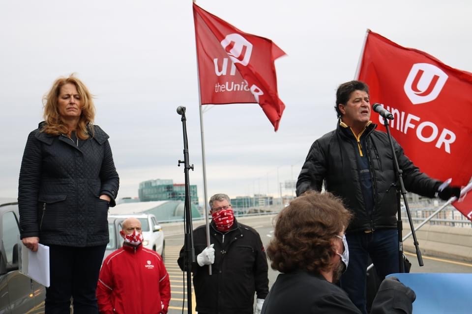 Jerry Dias with Katha Fortier speaking at a mic to a rally Unifor flags