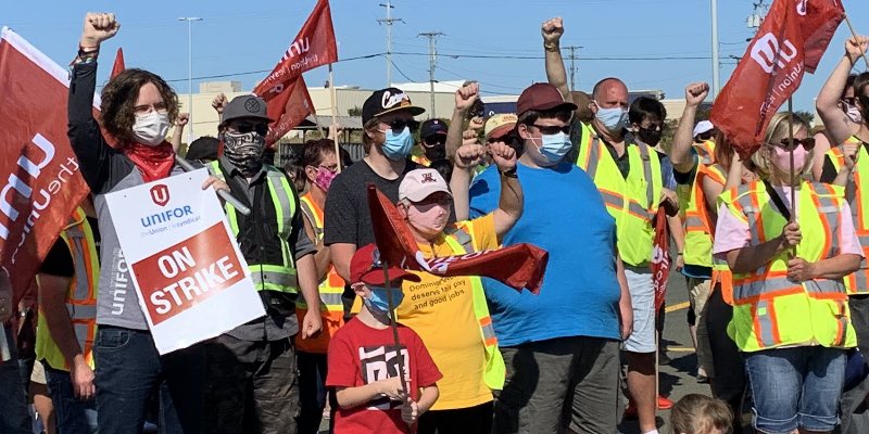 Members of Local 597 stand on a picket line holding flags and strike signs.
