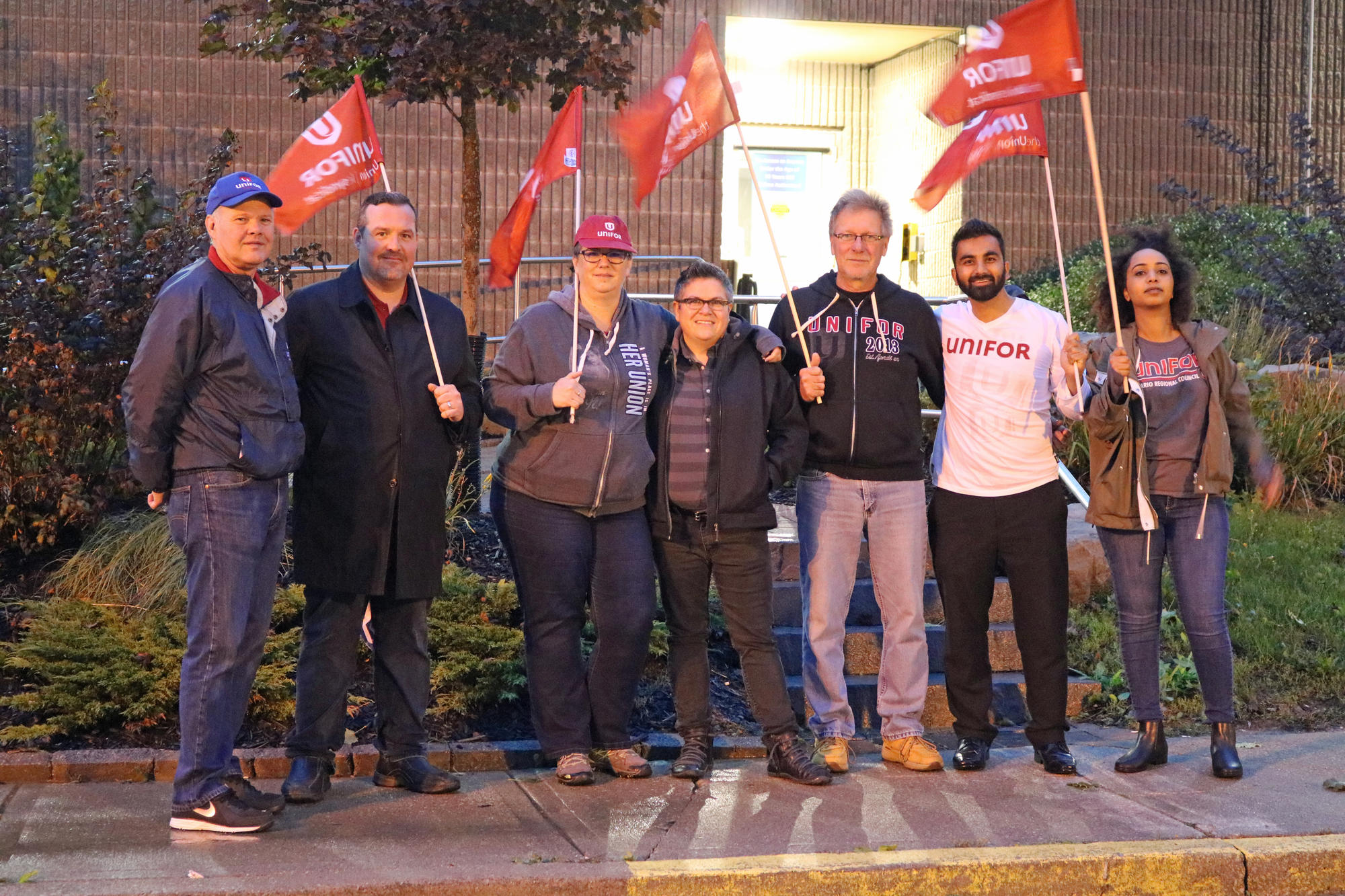 Seven Unifor members wave Unifor flags.