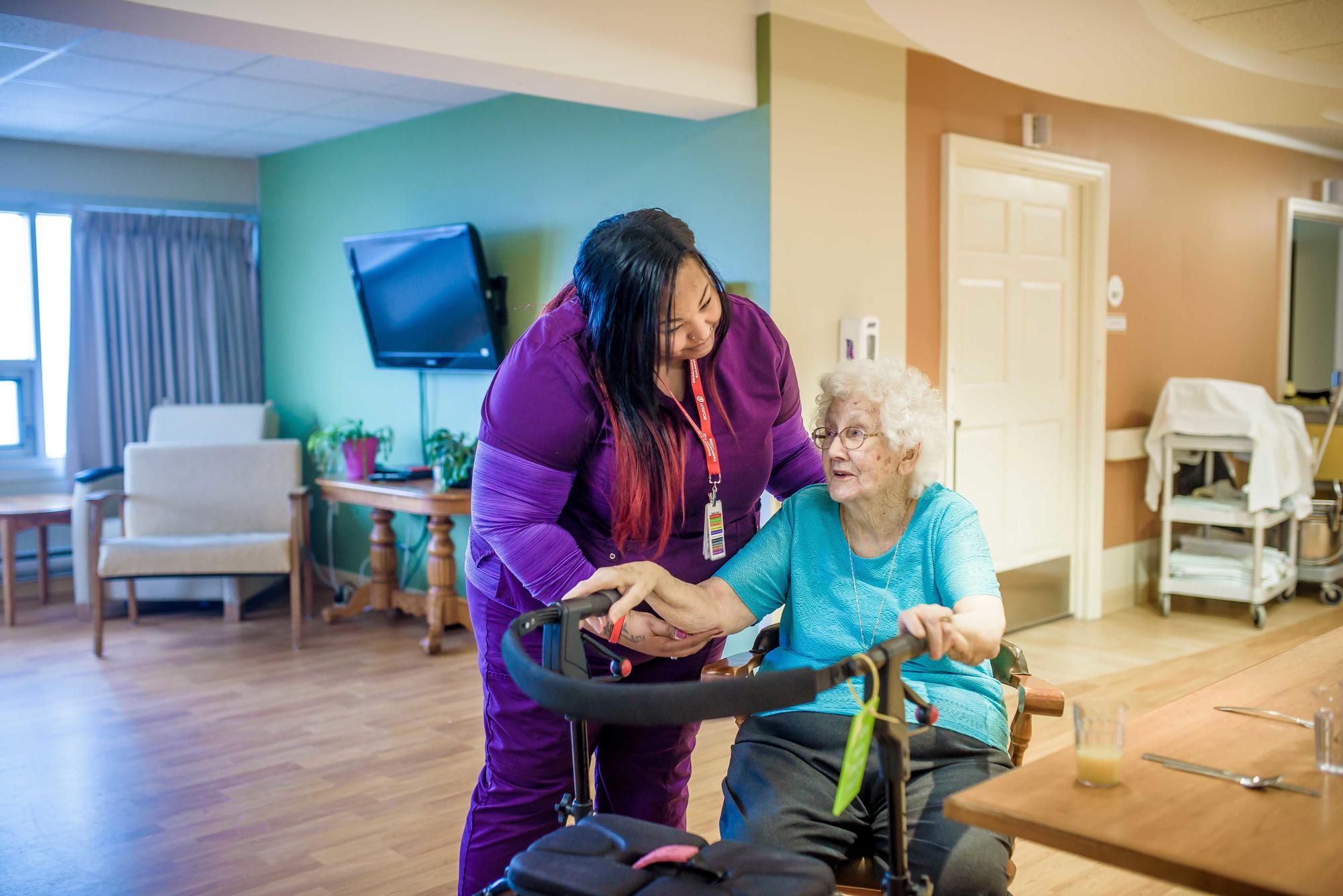 A health care worker assists an elderly resident in a long term care facility.