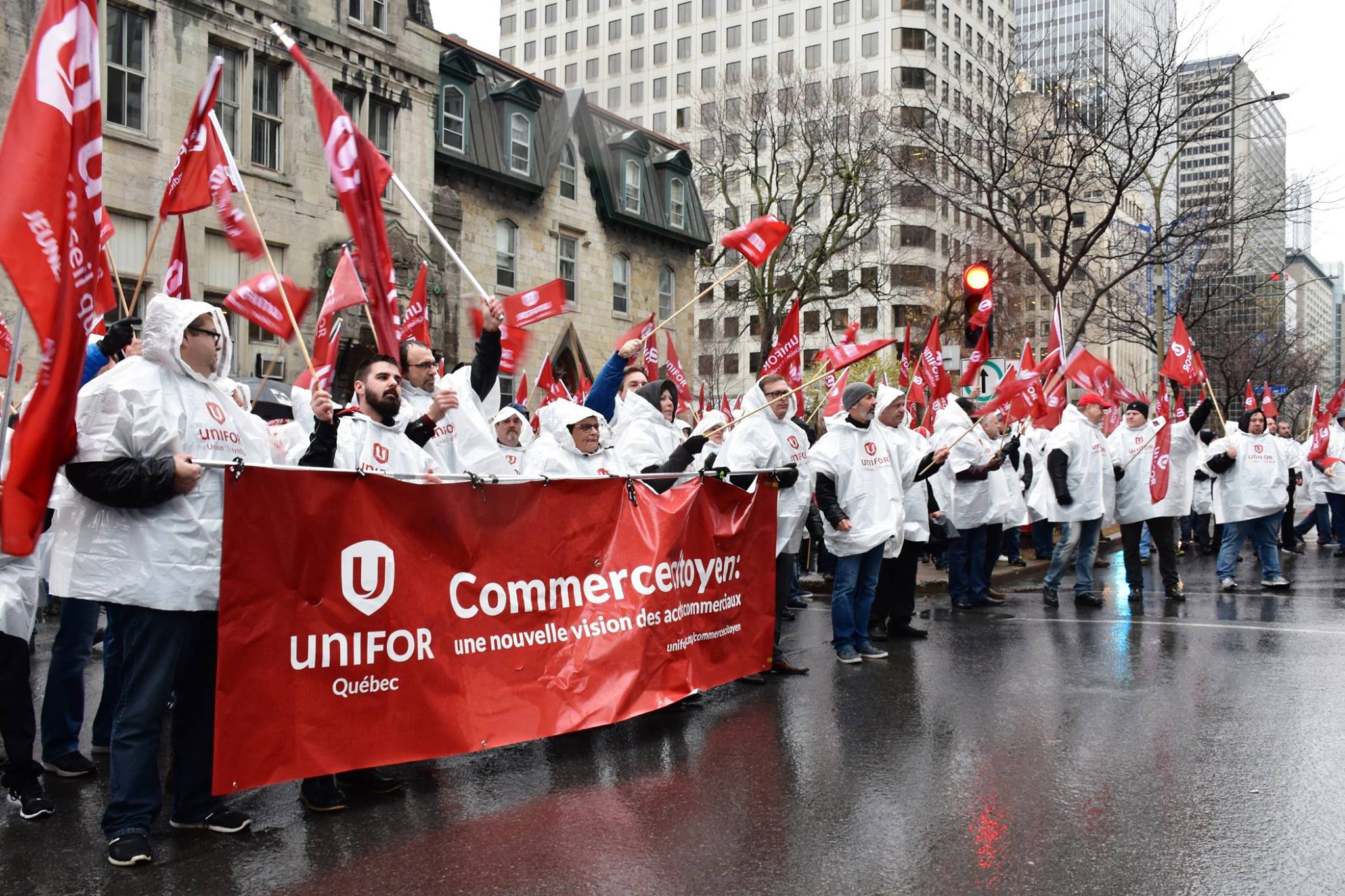Unifor activists in matching rain ponchos hold flags and a banner at a rally in Montreal.