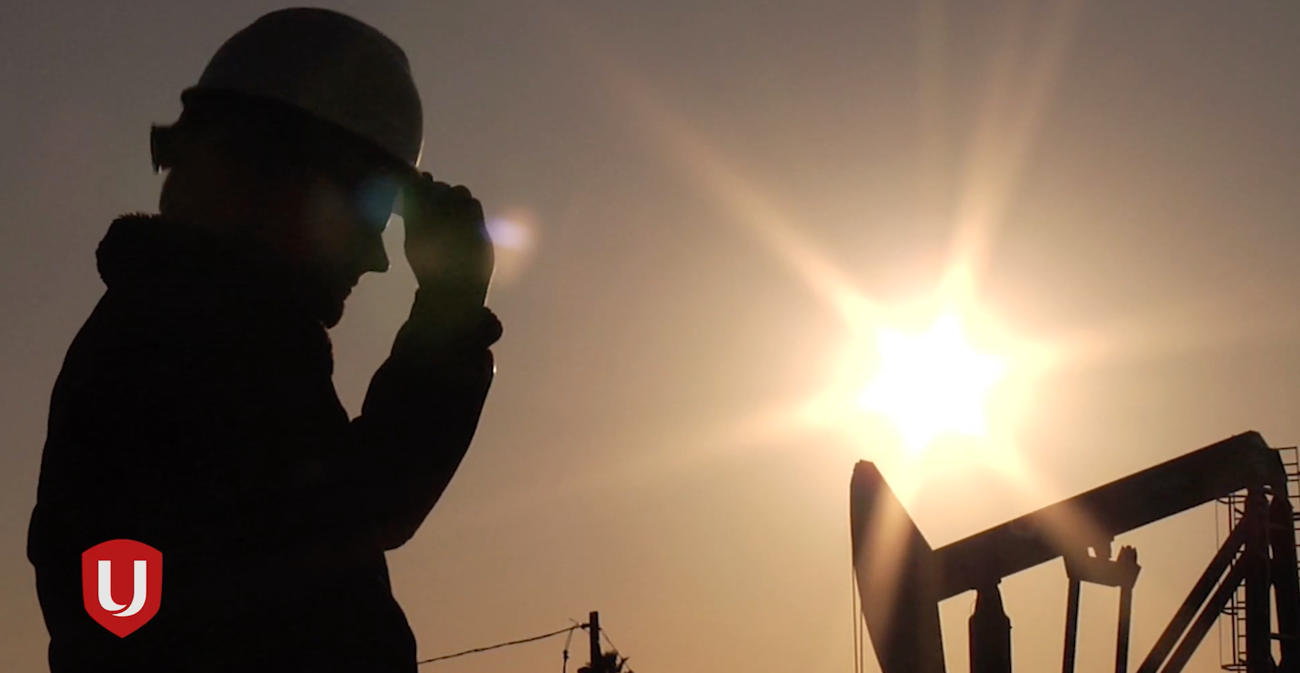 Side silhouette of a worker in a hardhat against a setting sun