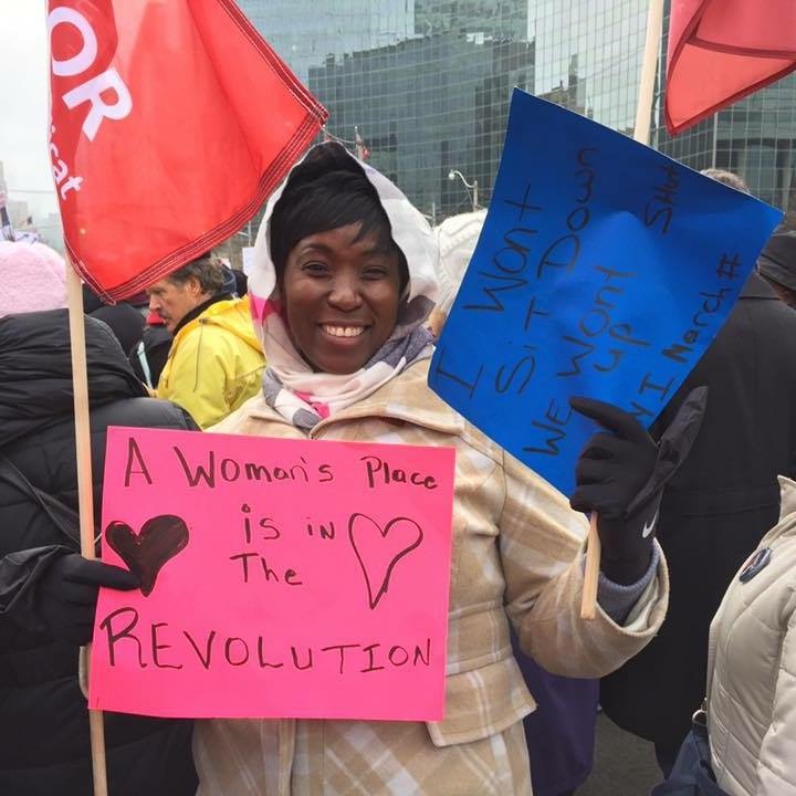 Unifor member Shereta Bowers holds a Unifor flag and a sign reading "A woman's place is in the revolution."