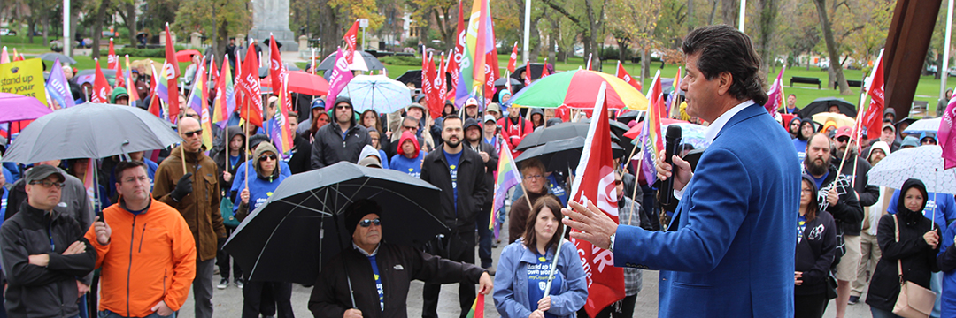 Jerry Dias speaks to a crowd holding Unifor flags and umbrellas.