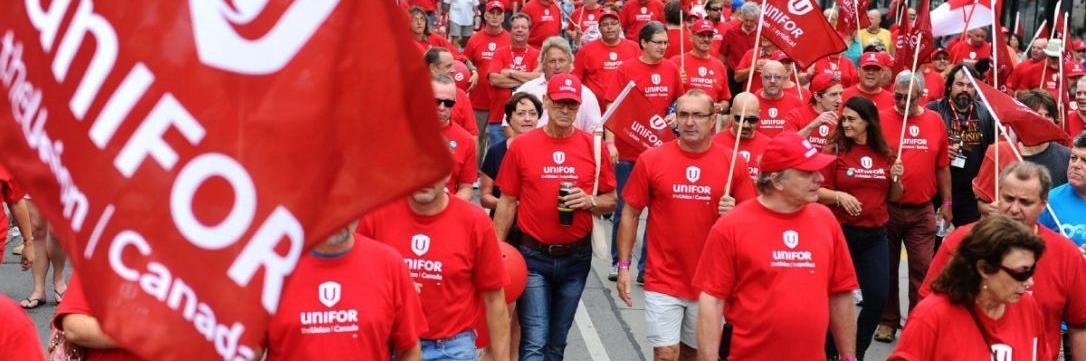 A large crowd of workers march wearing Unifor red t-shirts. 