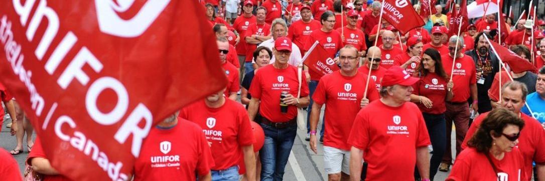 A large crowd of workers march wearing Unifor red t-shirts.