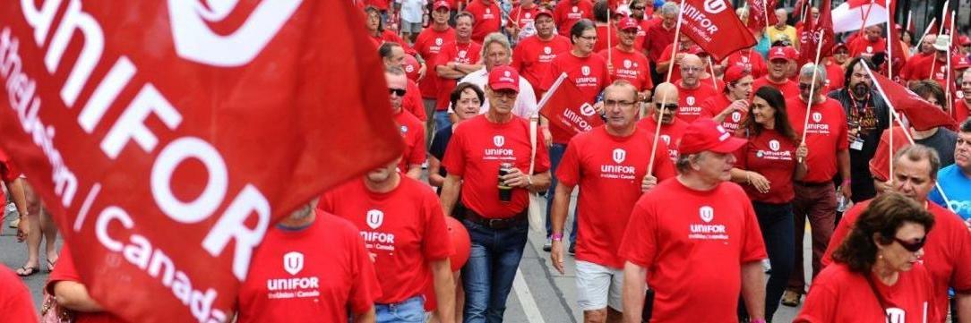 Bell members marching at a rally dressed in red Unifor shirts holding flags