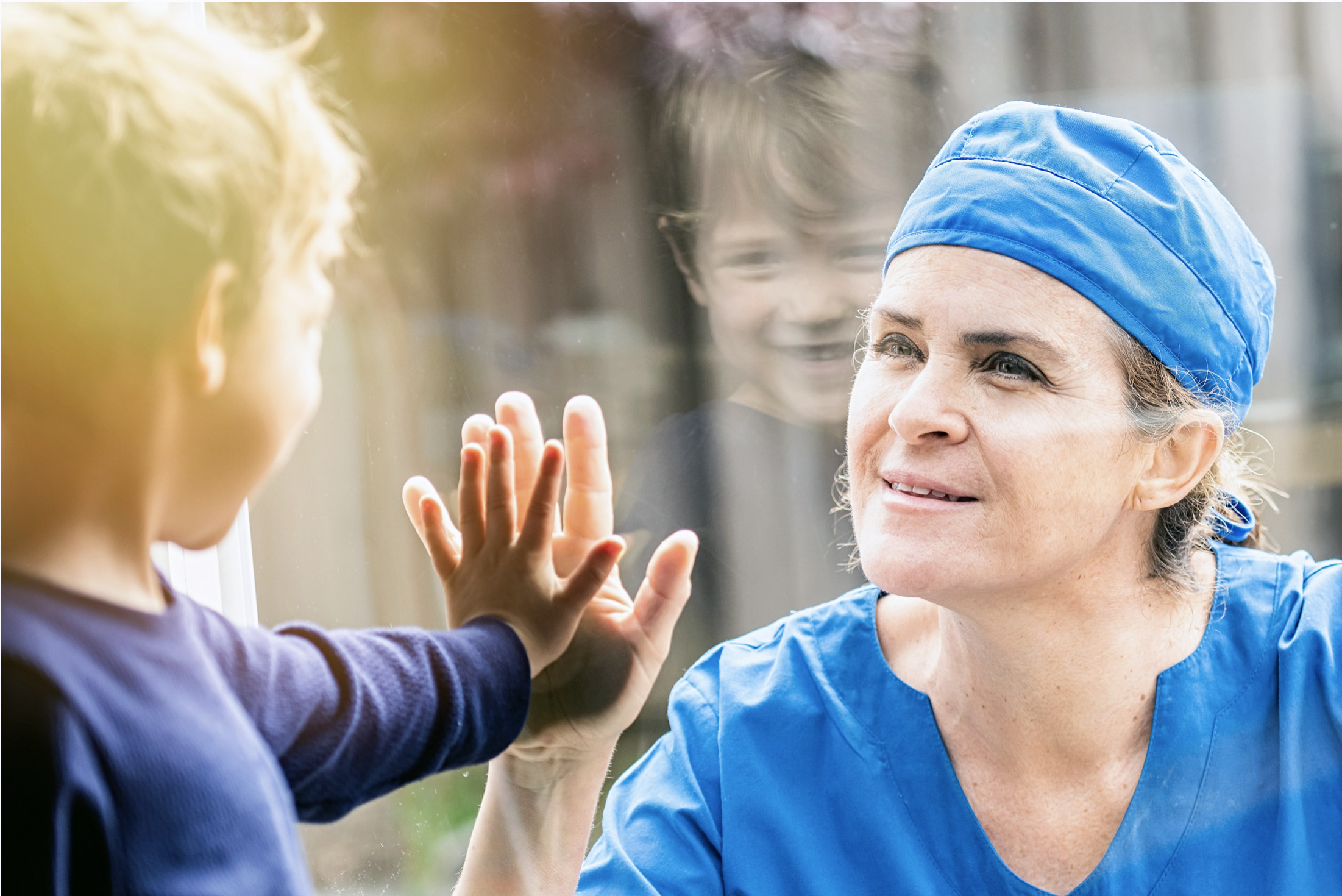a nurse looking through a window at a child both have their hand up to the glass touching..