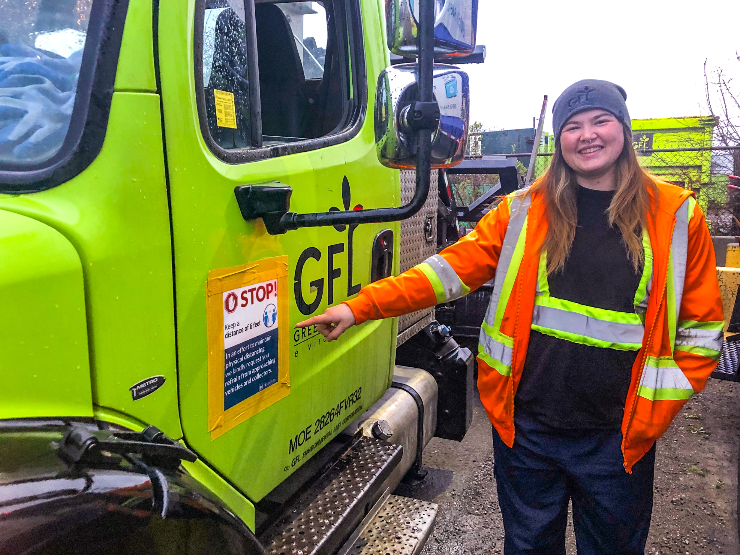 Waste vehicle operator in hi-vis gear smiling and pointing to their green truck
