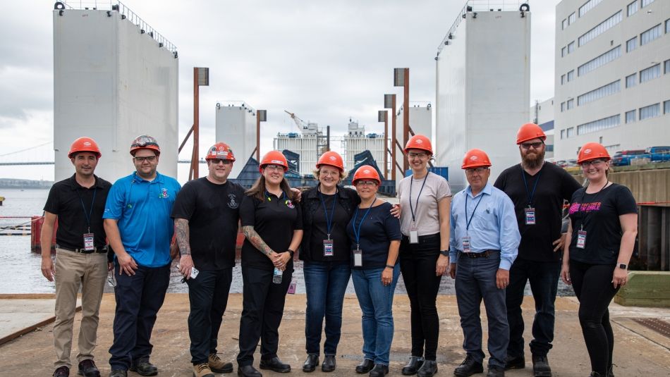 A group standing in a row wearing hardhats outside at Halifax Shipyard