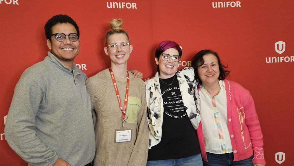 Four people posing in front of a Unifor banner