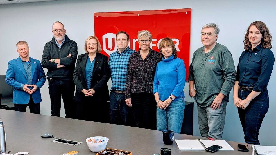 Huit personnes debout devant un drapeau d'Unifor accroché à un mur.