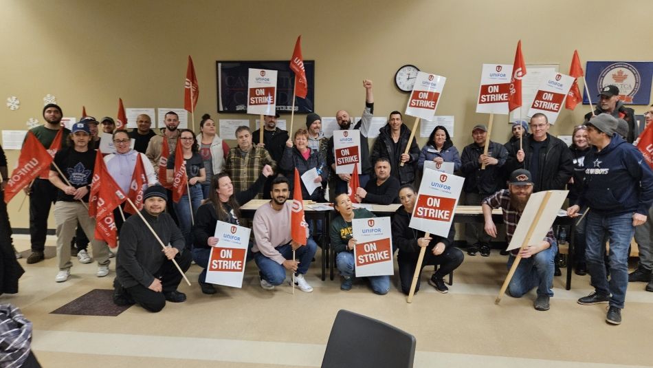 A group of people holding strike signs and red Unifor flags .