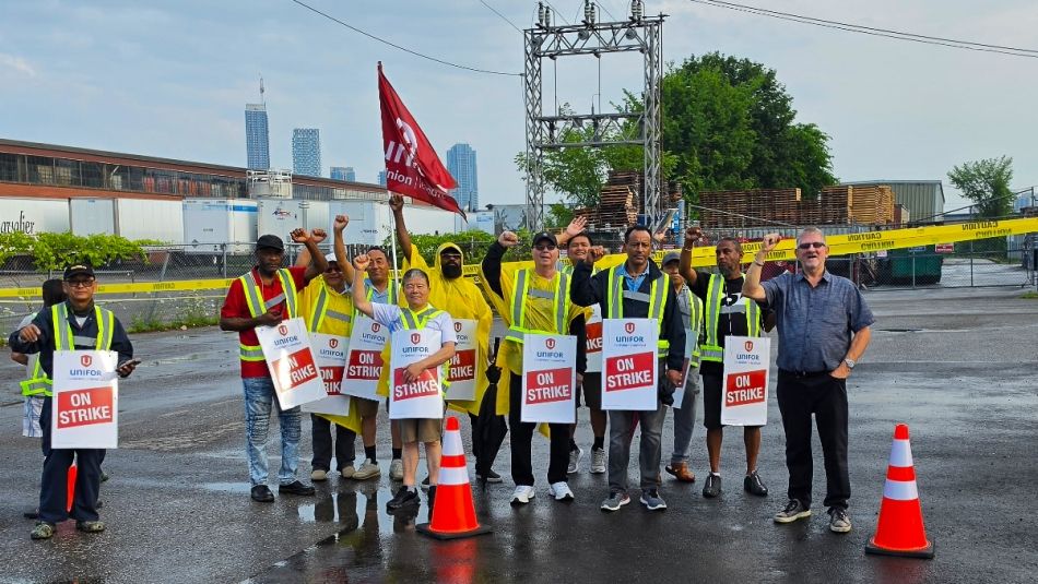 A group of people outside in the rain holding "On Strike" placcards