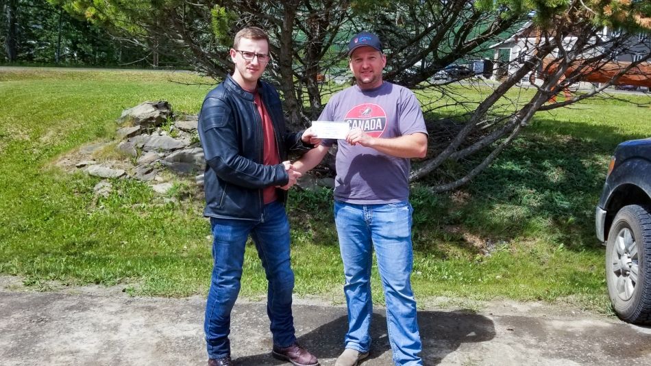 Two men holding outside a cheque and shaking hands