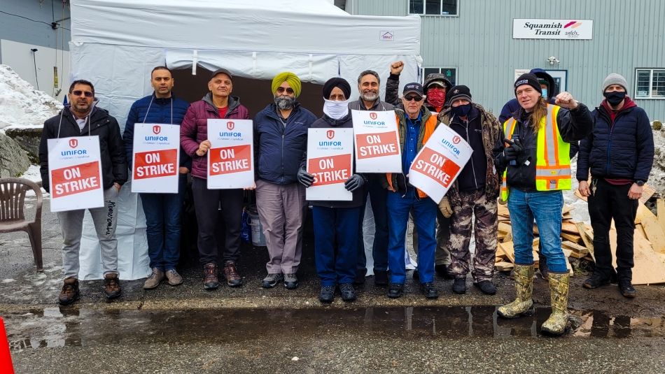 A line of Unifor members in front of a tent holding On Strike signs, some with fists in the air