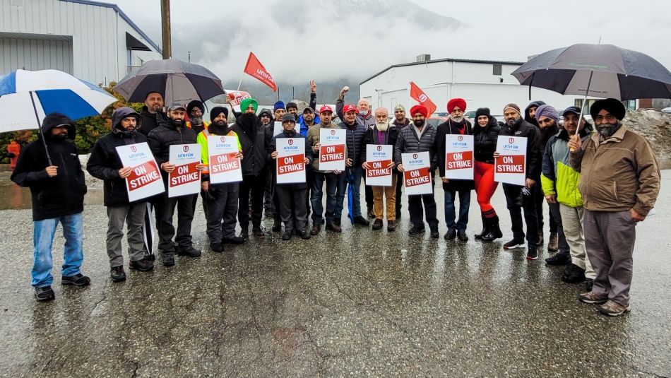 Large group of workers with On Strike signs posing for photo outdoors in wet weather