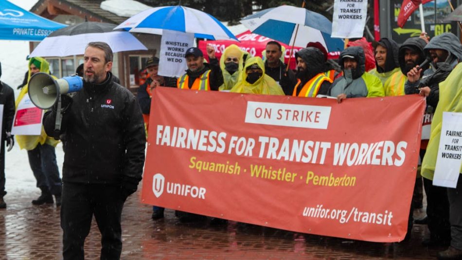 Man speaking into megaphone in front of crowd and Fairness for Transit Workers banner.