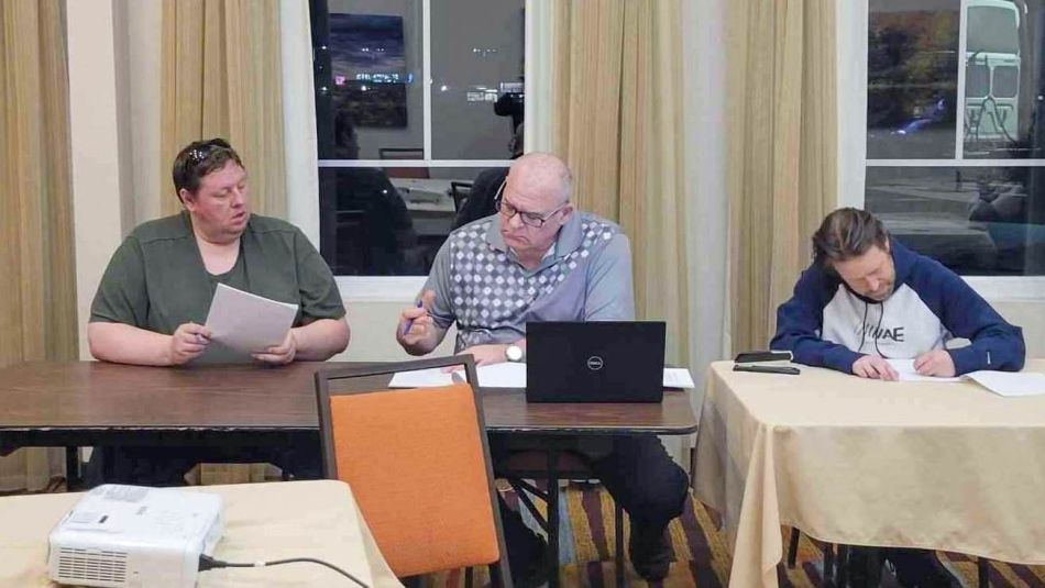 Three people sitting and working at a meeting room table.