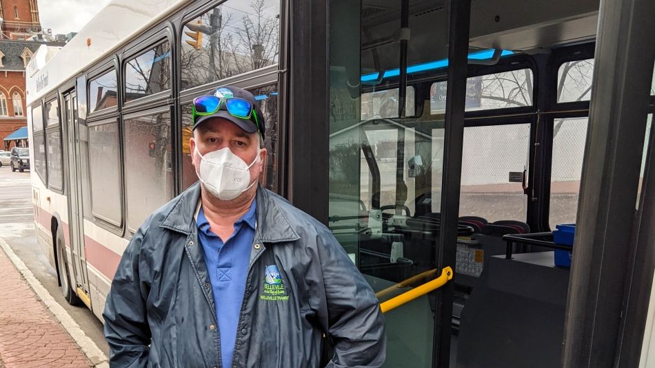 « Travailleur du service de transport en commun de la section locale 1839 d’Unifor à Belleville. » « Travailleur du service de transport en commun portant le masque, debout devant un autobus avec la porte ouverte. »