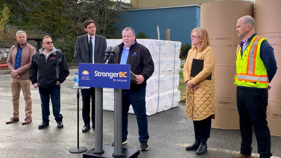 Person speaking from podium outside with government representatives to either side.