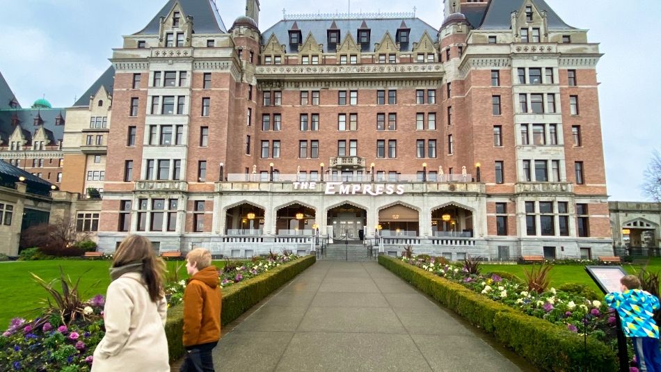 Empress Hotel building as seen from the street with two pedestrians walking past and an adolescent reading a lawn sign in the foreground